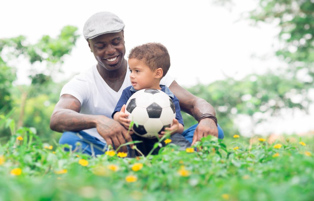 Un padre con su hijo pequeño con una pelota de fútbol sentados en la hierba